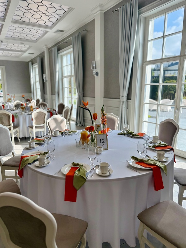 Okrągły stół z pomarańczowymi serwetkami i egzotycznymi kwiatami przy wysokich oknach