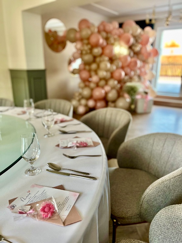 Baby shower - karta menu z upominkiem i różowo-złota ścianka balonowa w tle
